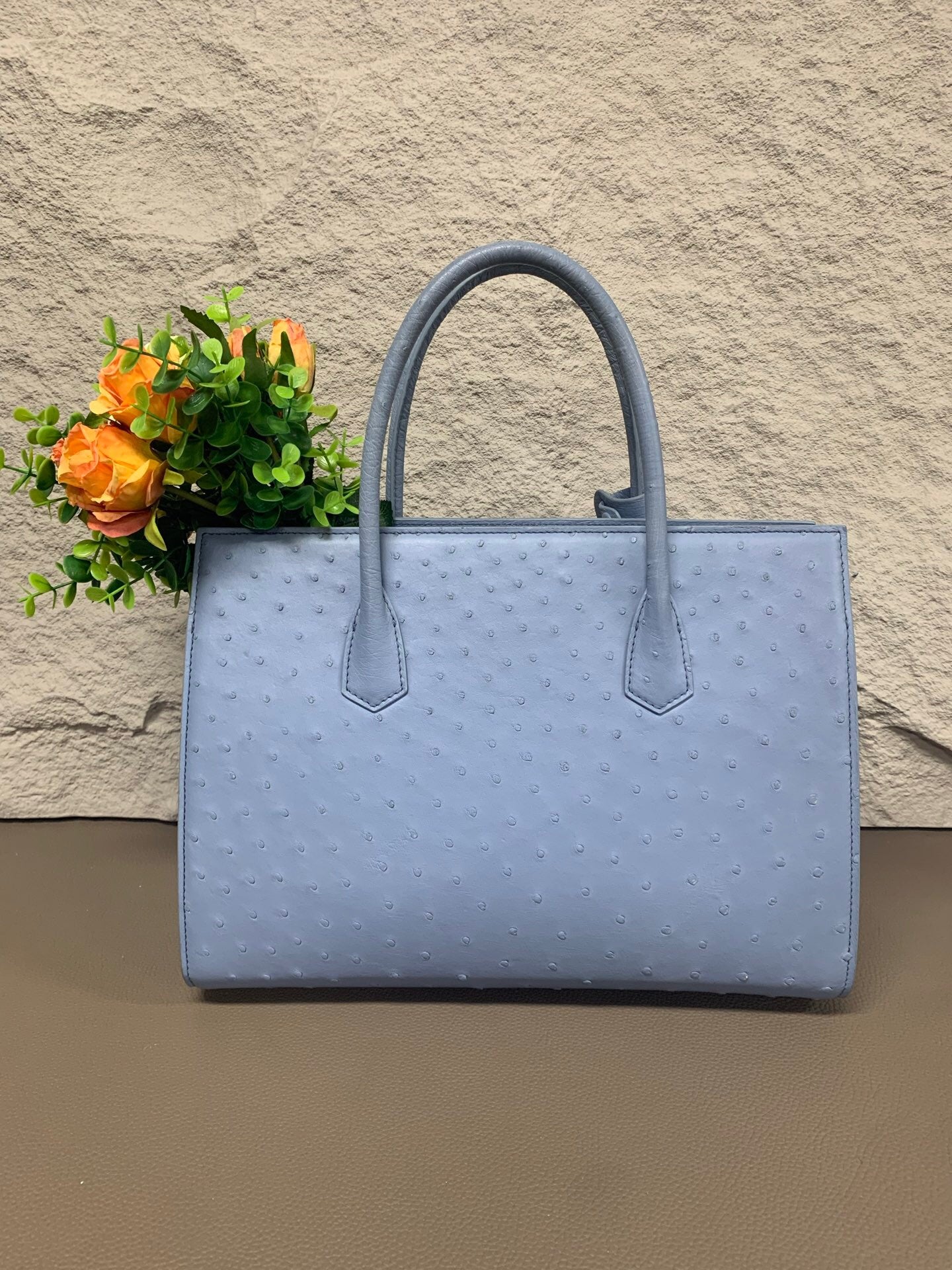 Women's ostrich skin leather handbag with top handle by Rossie Viren, showcasing a sleek, textured bag with gold accents.