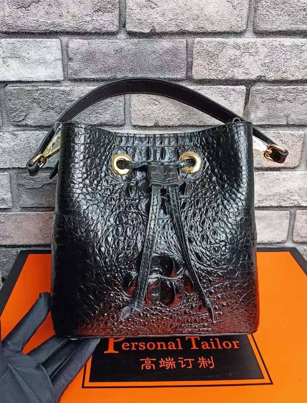 Crocodile leather bucket handbag by Rossie Viren with adjustable strap and gold-tone hardware on a neutral background.