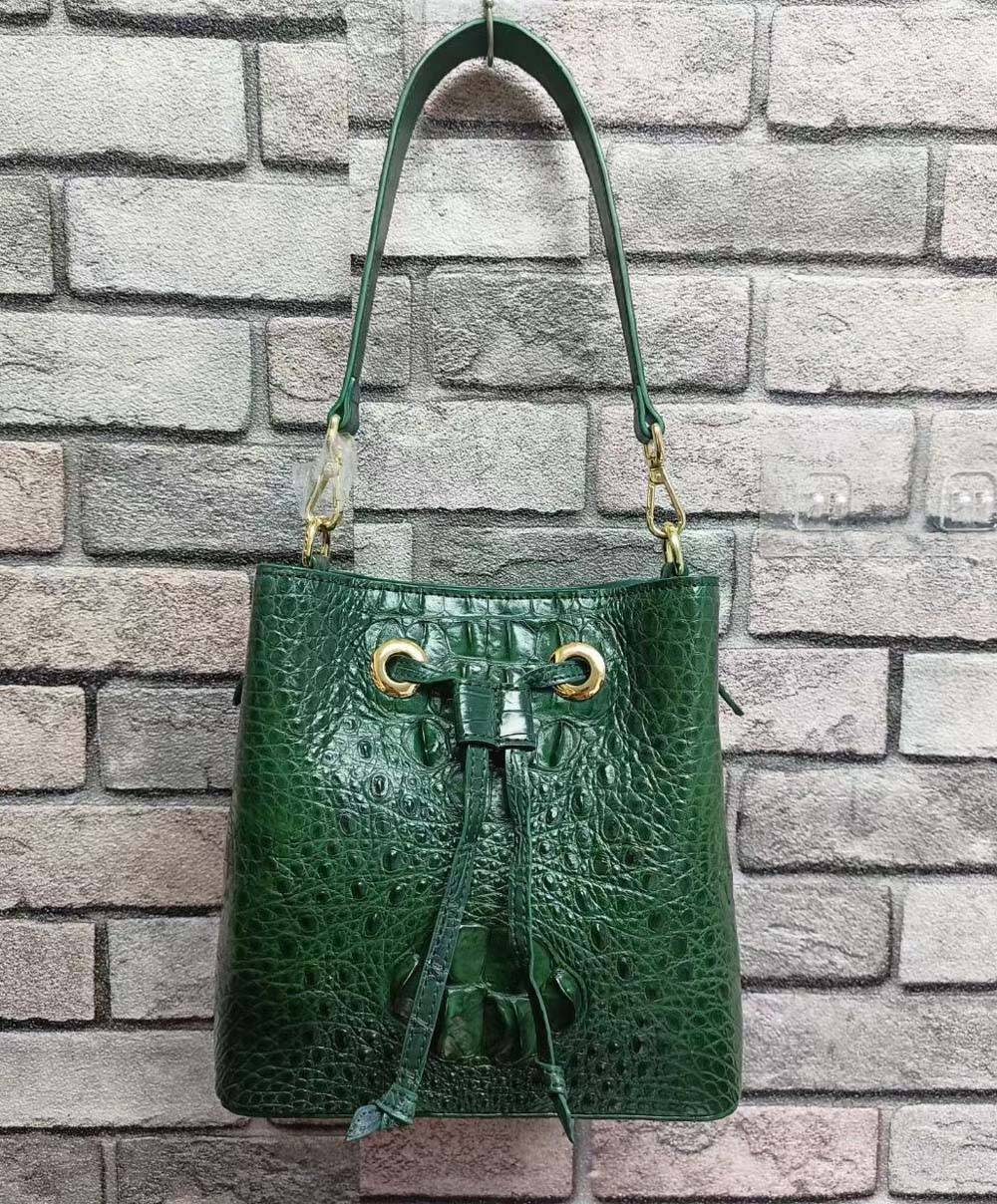 Rossie Viren crocodile leather bucket handbag with drawstring closure and adjustable strap on a plain background.